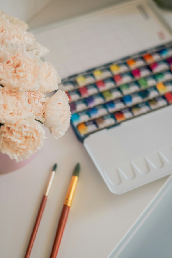 Watercolor paints and brushes on a cream background with flowers.